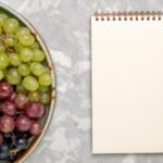 top-view-female-hands-cutting-lemon-with-knife-cornel-berries-grape-cinnamon-cutting-board-pluots-plant-gray-background_141793-52741